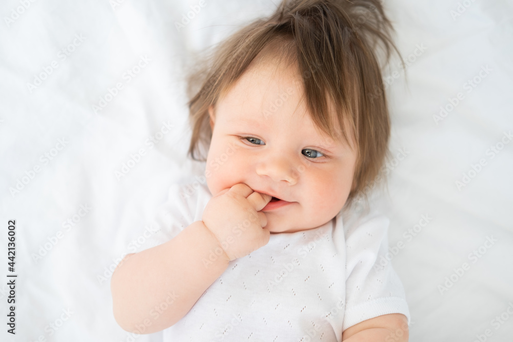 portrait of funny baby boy with finger in a mouth smiling and lying on a white bedding at home. portrait of funny baby boy with finger in a mouth smiling and lying on a white bedding at home.