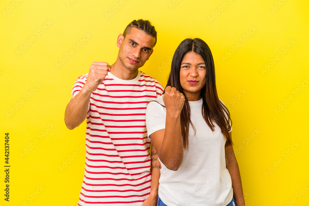 Young latin couple isolated on yellow background showing fist to camera, aggressive facial expression. Young latin couple isolated on yellow background showing fist to camera, aggressive facial expression.