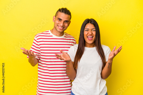 Young latin couple isolated on yellow background receiving a pleasant surprise, excited and raising hands.
