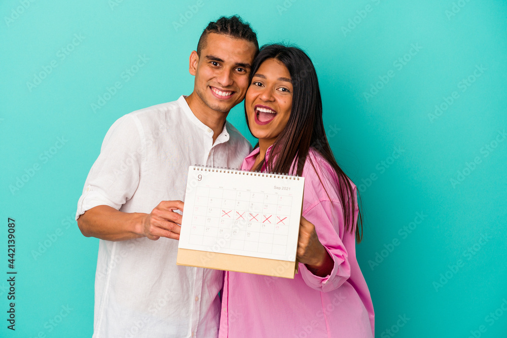 Young latin couple holding a calendar isolated on blue background Young latin couple holding a calendar isolated on blue background
