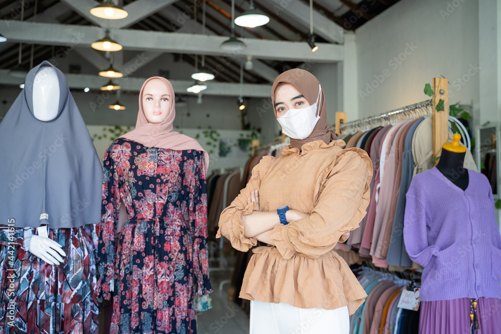 close up of a woman in a veil wearing a mask and crossing her arms stands inside a boutique shop