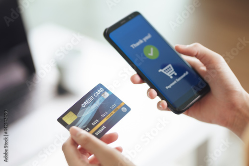 Young woman holding credit card and using smart phone for online shopping, internet banking, e-commerce, spending money, working from home concept