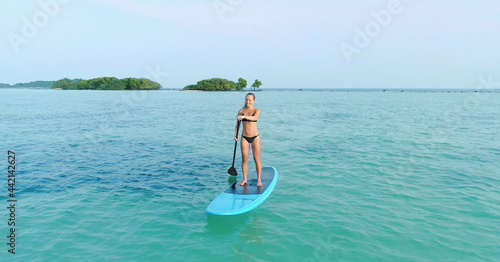 Aerial drone bird s eye view of man exercising sup paddle board in turquoise tropical clear waters  Thailand