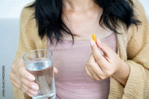 woman hand taking turmeric pill, girl hand holding turmeric powder in capsule or curcumin herb medicine with a glass of water, treatment for acid reflux problem photo