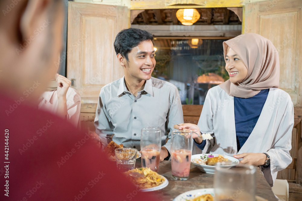 a man and a woman in veil chat while breaking their fast together in the dining room