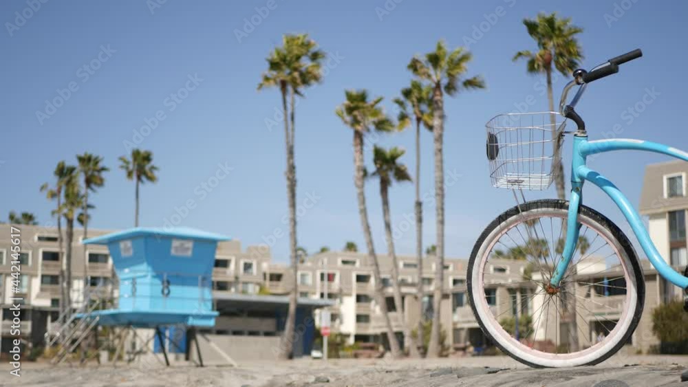 Blue bicycle, cruiser bike by ocean beach, pacific coast, Oceanside California USA. Summertime vacations, sea shore. Vintage cycle by beachfront houses, waterfront lodging. Lifeguard and palm trees. Blue bicycle, cruiser bike by ocean beach, pacific coast, Oceanside California USA. Summertime vacations, sea shore. Vintage cycle by beachfront houses, waterfront lodging. Lifeguard and palm trees.