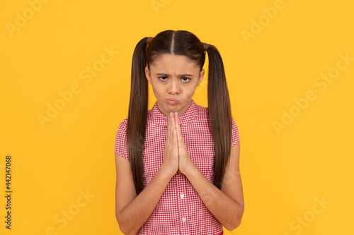 фотографія Praying girl child pray holding palms together in prayer gesture yellow backgrou