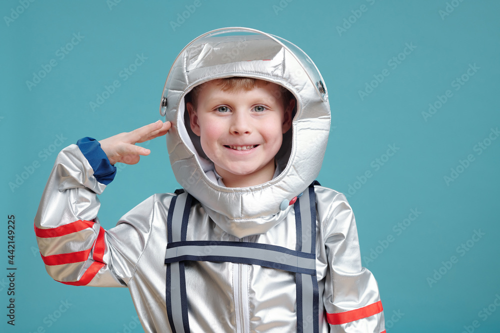 Happy cute little boy in space-suit keeping hand by temple Happy cute little boy in space-suit keeping hand by temple