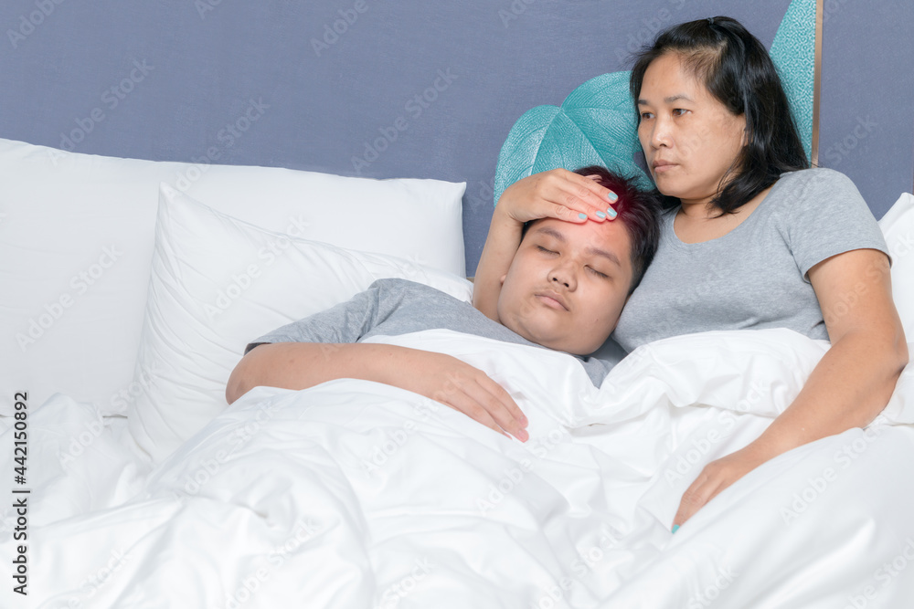 Mother puts her hand on forehead to measure the temperature of her son in bed.