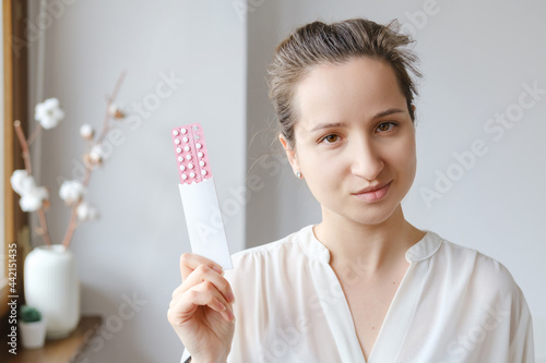Caucasian woman in white blouse holding hormonal oral contraceptives in a pink blister. Concept of Hormonal methods of birth control. Estrogen and Progestin hormonal balance.