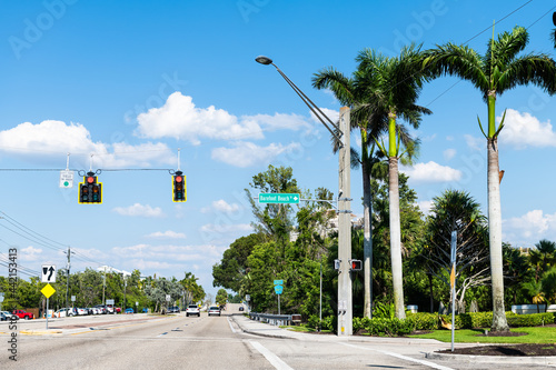 Palm trees on street road in Bonita Springs, Florida with sign for famous Barefoot Beach city town at day in Collier county with blue sky in spring photo