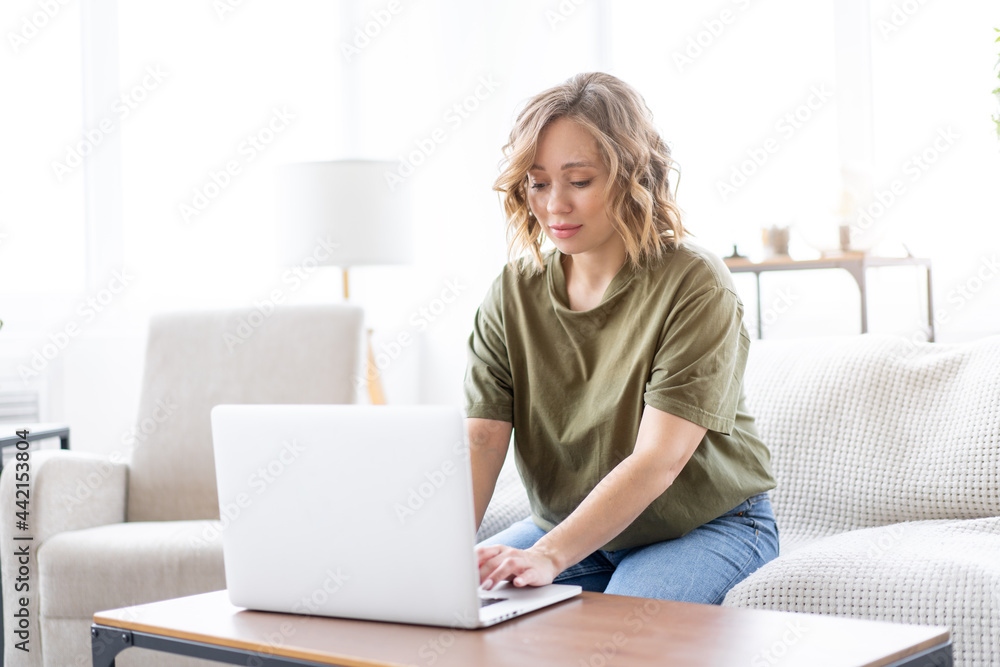 Woman using laptop computer while sitting sofa with big window on background at home interior Woman using laptop computer while sitting sofa with big window on background at home interior