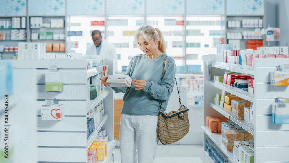 Pharmacy Drugstore: Portrait of a Beautiful Senior Woman Choosing to Buy Medicine, Drugs, Vitamins. Apothecary Full of Health Care Products, Supplement Bottles, Beauty Packages with Modern Design