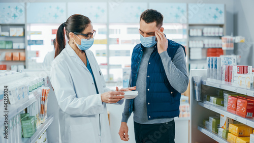 Covid-19 Pharmacy Wearing Face Masks: Professional Pharmacist Helping Handsome Male Customer with Medicine Recommendation, Talking. Drugstore with Full of Drugs, Pills, Health Care, Sport Products