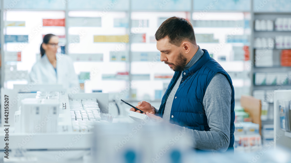 Pharmacy Drugstore: Portrait of Handsome Young Caucasian Man Using Smartphone, Searching to Purchase Best Medicine, Drugs, Vitamins. Shelves full of Health Care, Wellness, Sports Supplements
