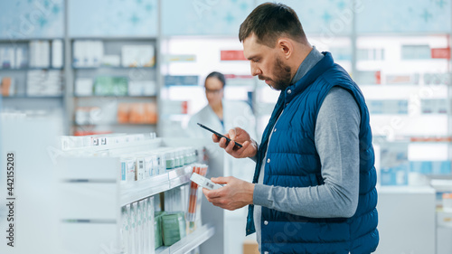 Obraz na plátně Pharmacy Drugstore: Portrait of Handsome Young Caucasian Man Using Smartphone, Searching to Purchase Best Medicine, Drugs, Vitamins