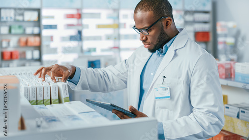 Pharmacy  Portrait of Professional Black Pharmacist Uses Digital Tablet Computer  Checks Inventory of Medicine  Drugs  Vitamins  Health Care Products on a Shelf. Pharmacist in Drugstore Store