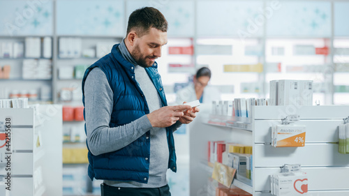 Obraz na plátně Pharmacy Drugstore: Portrait of a Handsome Young Man Choosing to Buy Medicine, Drugs, Vitamins