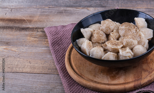 Cooked dumplings in a black round tarek sprinkled with hot pepper on a wooden background photo