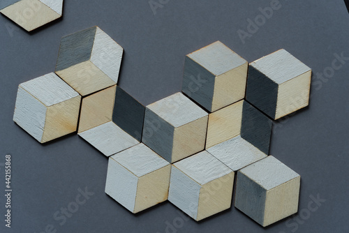 3d wooden cubes (hexagons) hand painted in white and various shades of gray acrylic paint, loosely arranged on a medium gray paper background, and photographed from above in a flat lay style with ambi