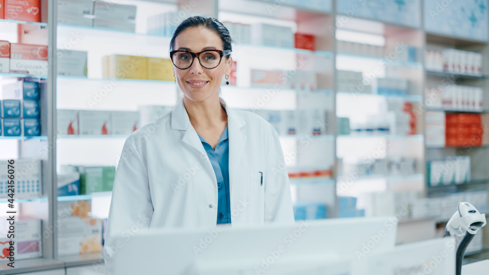 Pharmacy Counter: Portrait of Beautiful Professional Caucasian Female Pharmacist Working on Computer, Looks at Camera Smiling Charmingly. Drugstore Store with Shelves Health Care Products