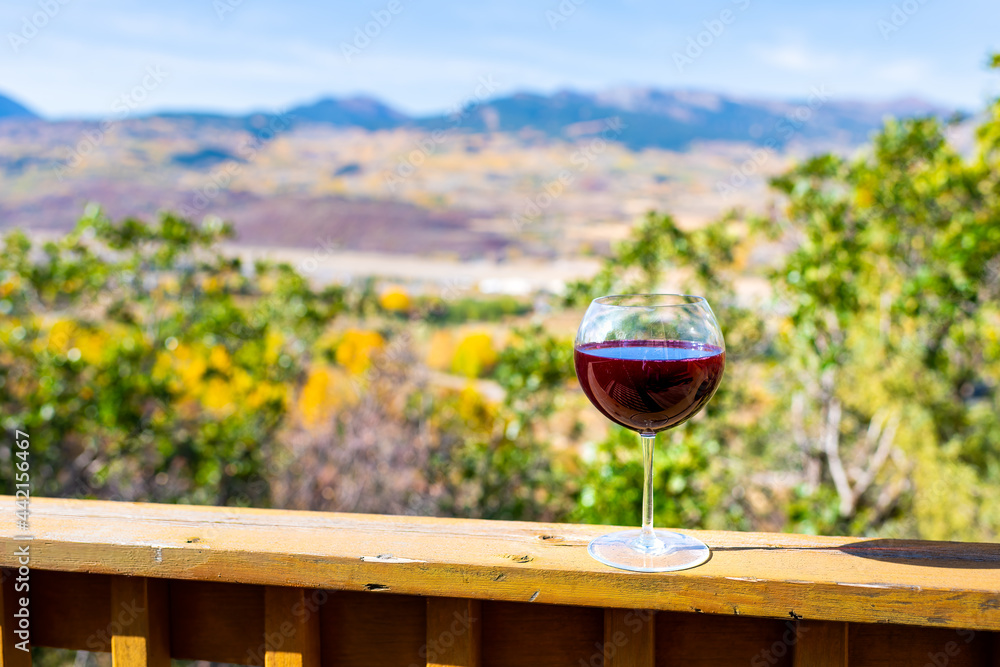 Red wine glass crystal on terrace railing and bokeh background view of autumn foliage yellow trees in Aspen, Colorado rocky mountains