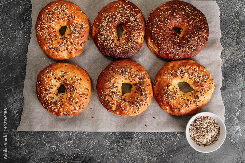 Appetizing and crunchy bagels with sesame and flax seeds. Homemade hot baked goods. Bagels on baking paper on a gray concrete background. Cook at home. Top view. Copy space © yusev