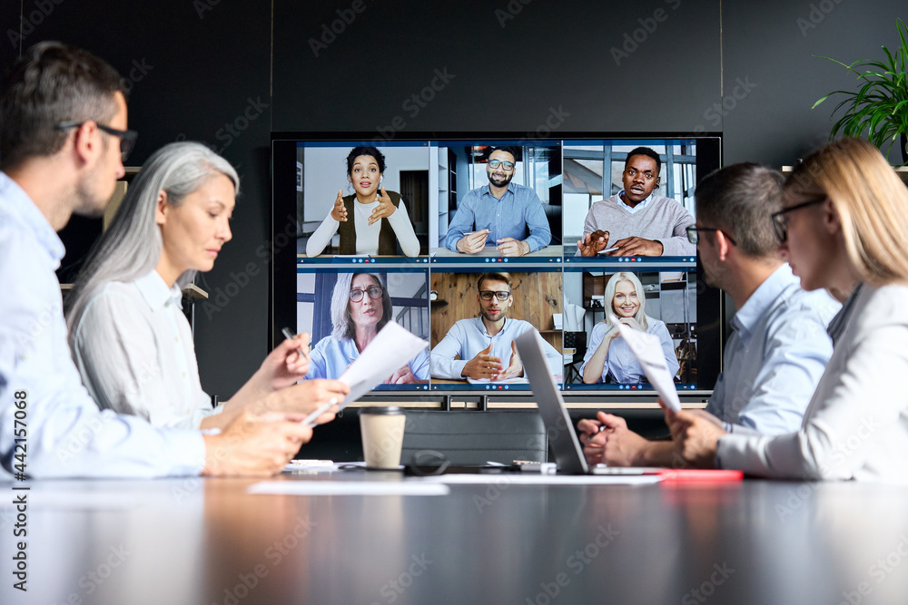 Global corporation online videoconference in meeting room with diverse people sitting in modern office and multicultural multiethnic colleagues on big screen monitor. Business technologies concept. - obrazy, fototapety, plakaty 