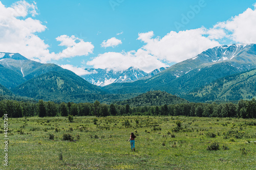 Young girl runs on green meadows in front of the high mountains