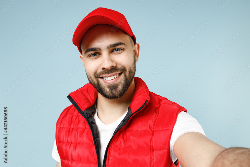 Close up professional delivery guy employee man in red cap white T-shirt uniform workwear work as dealer courier doing selfie isolated on pastel blue color background studio portrait. Service concept. Close up professional delivery guy employee man in red cap white T-shirt uniform workwear work as dealer courier doing selfie isolated on pastel blue color background studio portrait. Service concept.