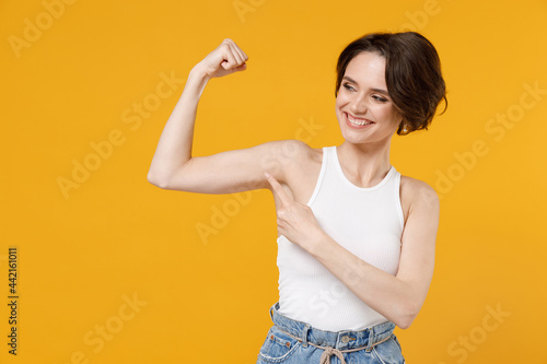 Young strong sporty fitness woman 20s with bob haircut wearing white tank top point finger on biceps muscles on hand demonstrate strength power isolated on yellow background People lifestyle concept