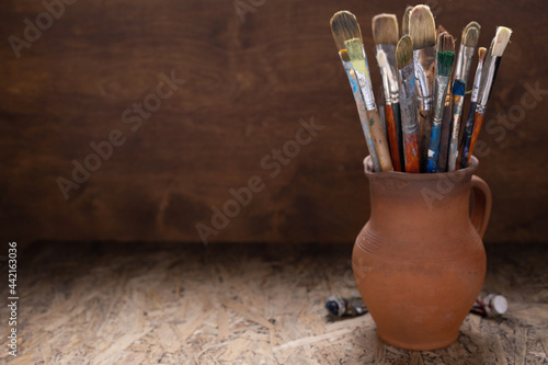 Paint brush in clay jug and used tubes on wooden table background . Paintbrush for art painting