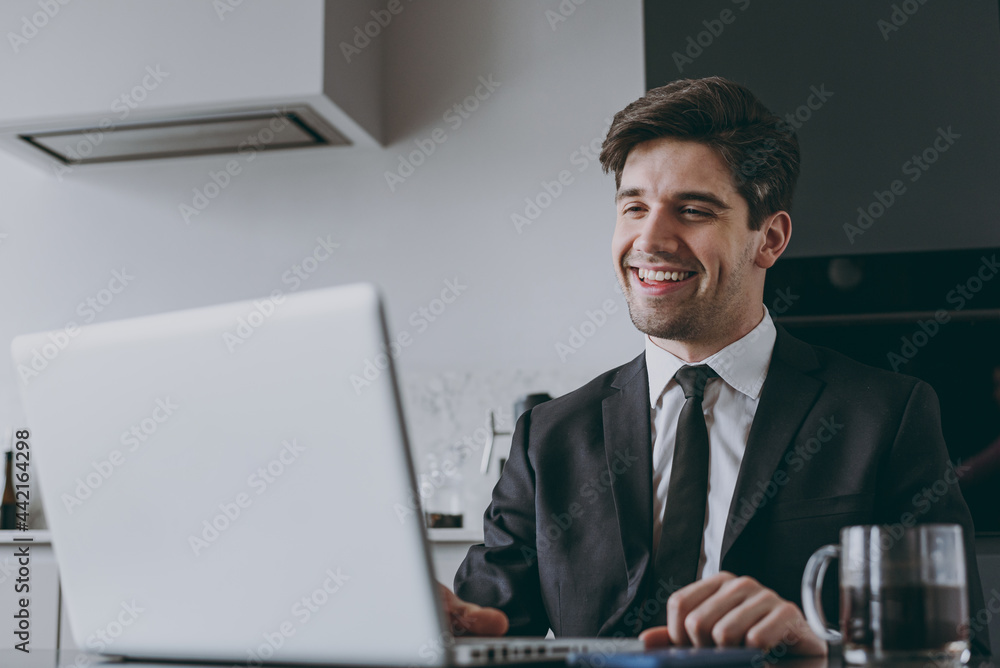 Bottom view happy young employee business man corporate lawyer in black suit shirt tie using laptop pc computer browsing working on internet sit at kitchen table coffee People career ladder concept Bottom view happy young employee business man corporate lawyer in black suit shirt tie using laptop pc computer browsing working on internet sit at kitchen table coffee People career ladder concept