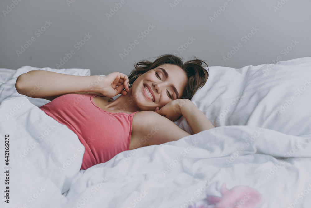 Calm young fun smiling positive caucasian woman 20s wearing pajamas lying on bed wrap covered under blanket duvet on pillow stretching resting relax at home. Good mood night morning bedtime concept Calm young fun smiling positive caucasian woman 20s wearing pajamas lying on bed wrap covered under blanket duvet on pillow stretching resting relax at home. Good mood night morning bedtime concept