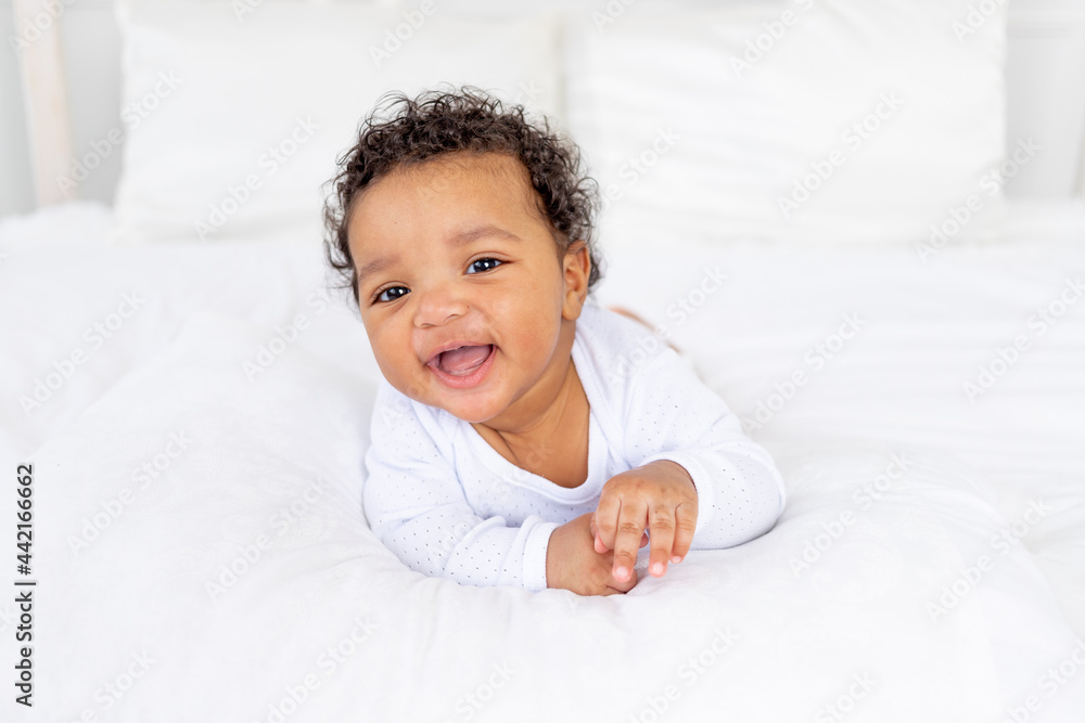 smiling African-American little baby on white bed in bedroom laughing smiling African-American little baby on white bed in bedroom laughing