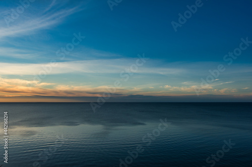 A sky with haze turning into cloudy on the horizon, during the white nights at sunset over a calm sea with fine ripples.