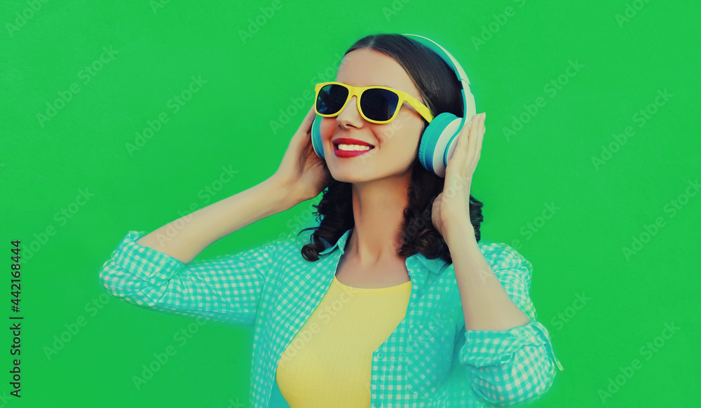 Portrait close up of happy smiling young woman listening to music in wireless headphones on a green background
