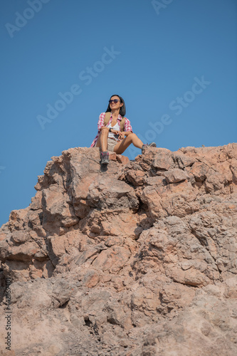 fit young woman hiking in the mountains standing on a rocky summit ridge with backpack and pole looking out over landscape. hiker with backpack relaxing on top of a mountain and enjoying valley view.