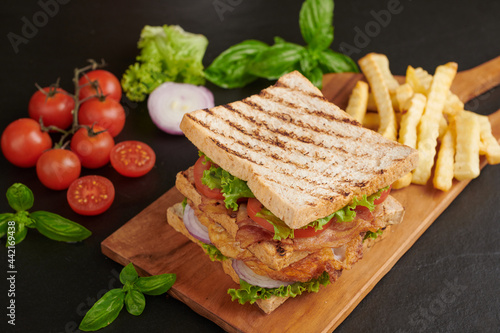 Club-sandwich with french fries. Sandwich with bacon, fried egg. Grilled and pressed toast with bacon, fried egg, tomato and lettuce served on wooden cutting board.