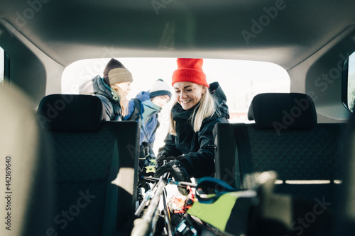 Leende kvinna lägger in skidor och stavar i bil photo
