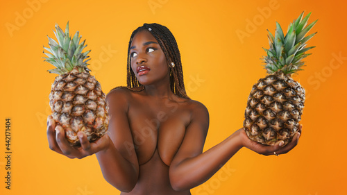 Young sexy woman happy smiling posing on background with pineapple who cover her breast photo