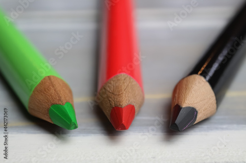 Fotografie Closeup of isolated colorful green, red and black crayons on wood background - k