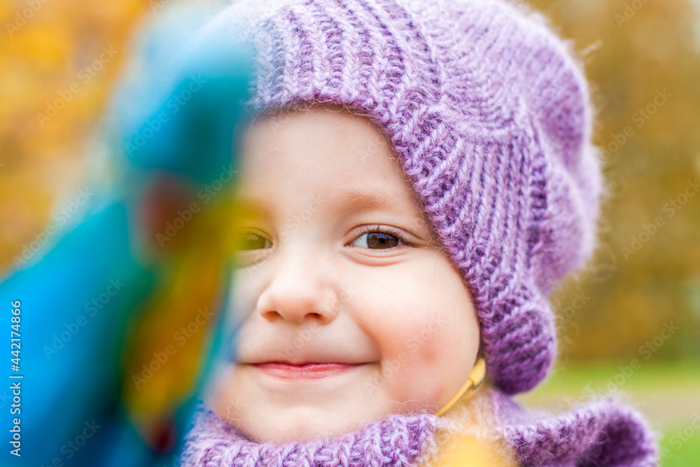 A child in a purple knitted hat and scarf. Portrait of a child against the background of autumn trees. Cute smiling boy. A child in a purple knitted hat and scarf. Portrait of a child against the background of autumn trees. Cute smiling boy.