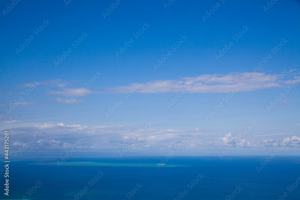 Poster of the blue sky over blue ocean.  Blue wallpaper. Ocean view from the top of Cook Island in Australia on the Great Barrier Reef. Turquoise water with white shallows. Sunny tropical day. 