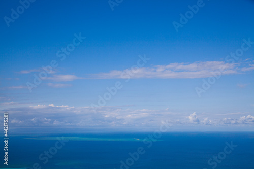 Poster of the blue sky over blue ocean. Blue wallpaper. Ocean view from the top of Cook Island in Australia on the Great Barrier Reef. Turquoise water with white shallows. Sunny tropical day. 