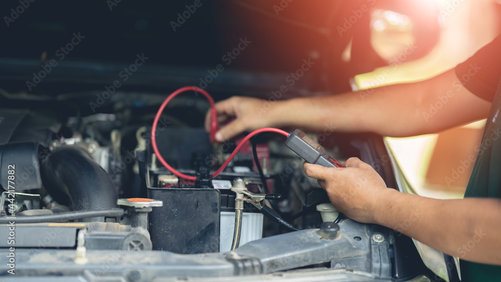 A mechanic is using a voltmeter to measure the current at the car battery. A mechanic is using a voltmeter to measure the current at the car battery.