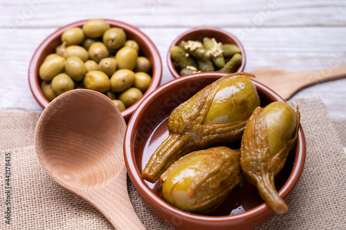 Seasoned olives, pickles in vinegar and Almagro aubergines in a brown bowl on a straw coaster photo