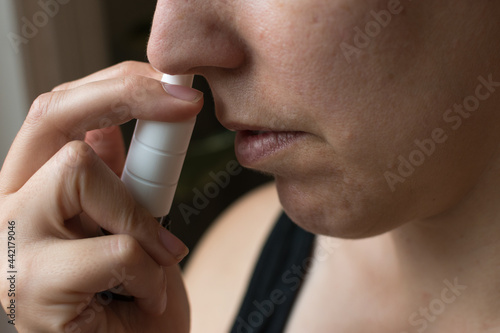 Woman in profile taking an allergy nasal spray; female is 40 years old