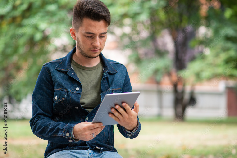 Man using his tablet while sitting on a banch in the park Man using his tablet while sitting on a banch in the park