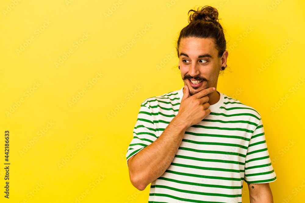 Young caucasian man with long hair isolated on yellow background touching back of head, thinking and making a choice.
